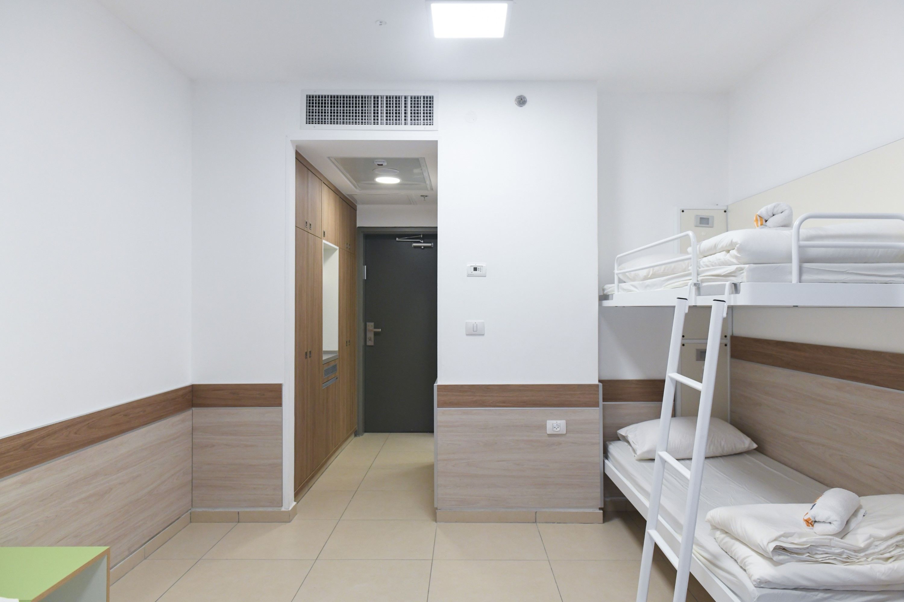 A hotel room with a bunk bed, a wooden wardrobe, and a small table.