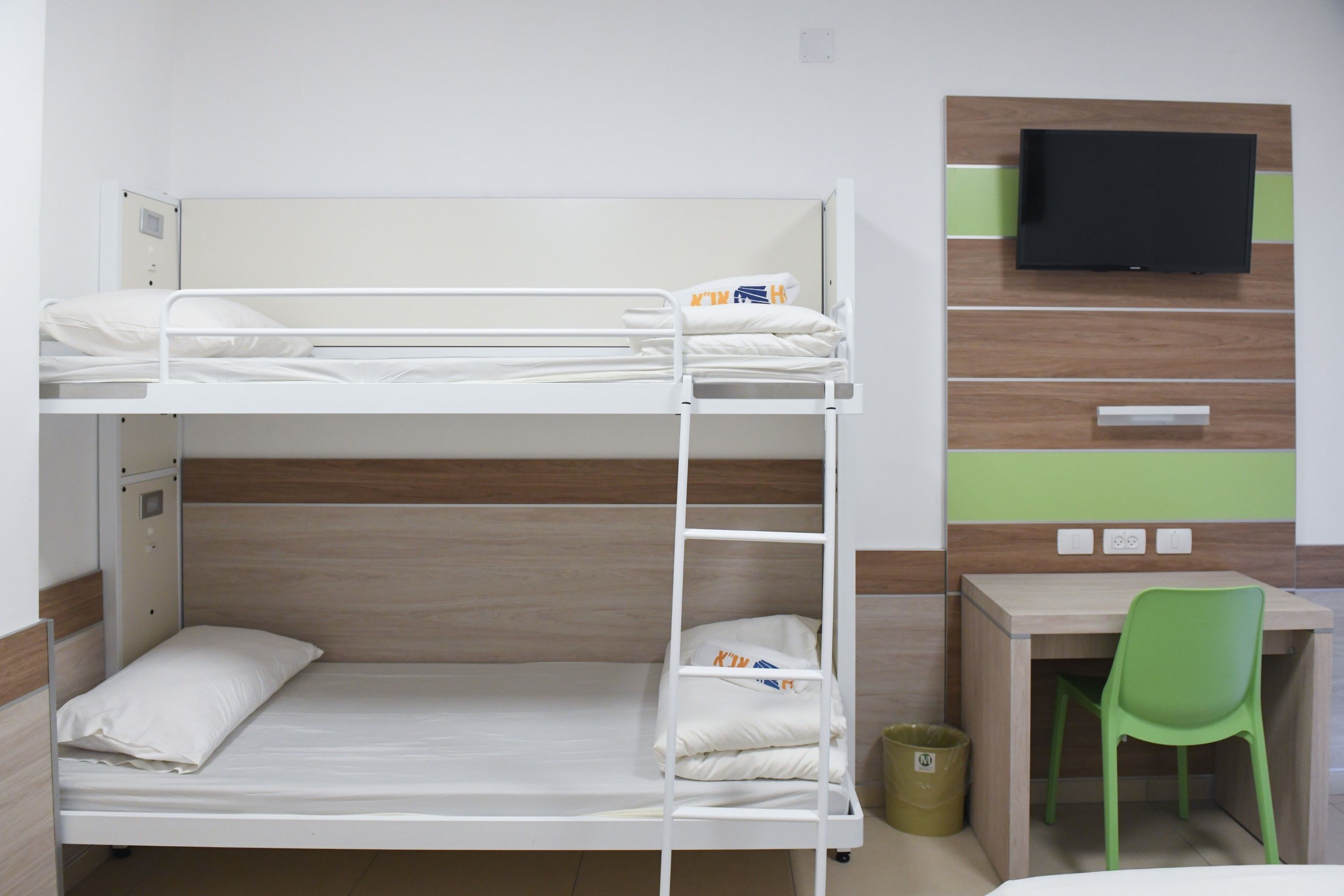 A bunk bed with a desk and chair, a television, and a trash can.