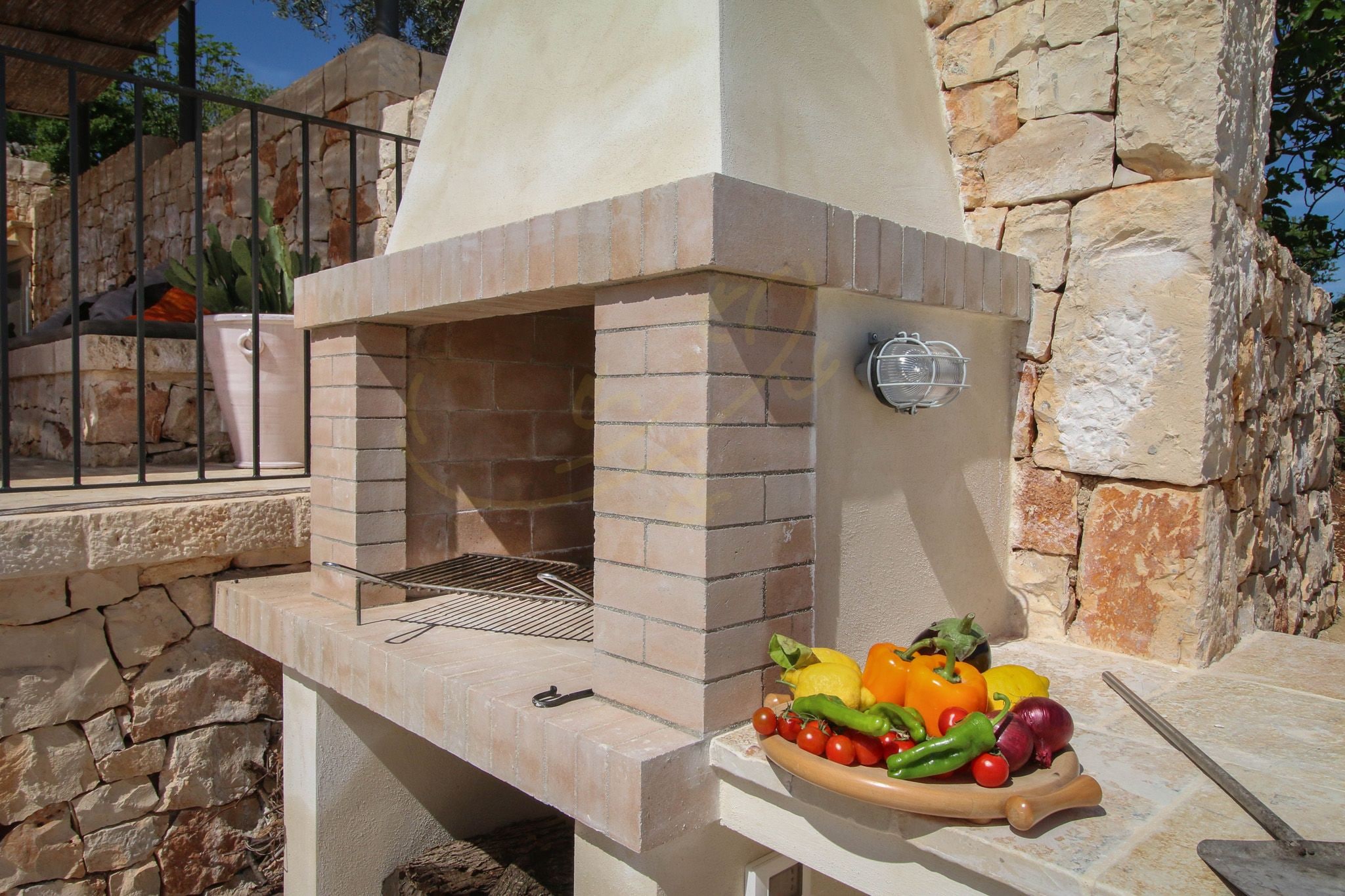 An outdoor brick oven with a grill and a variety of vegetables on a wooden board.