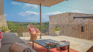 A balcony with a wicker chair, a table with a towel, and a view of a stone building and greenery. - TD Casale Terranova Stone Farmhouse with Pool (Monopoli)