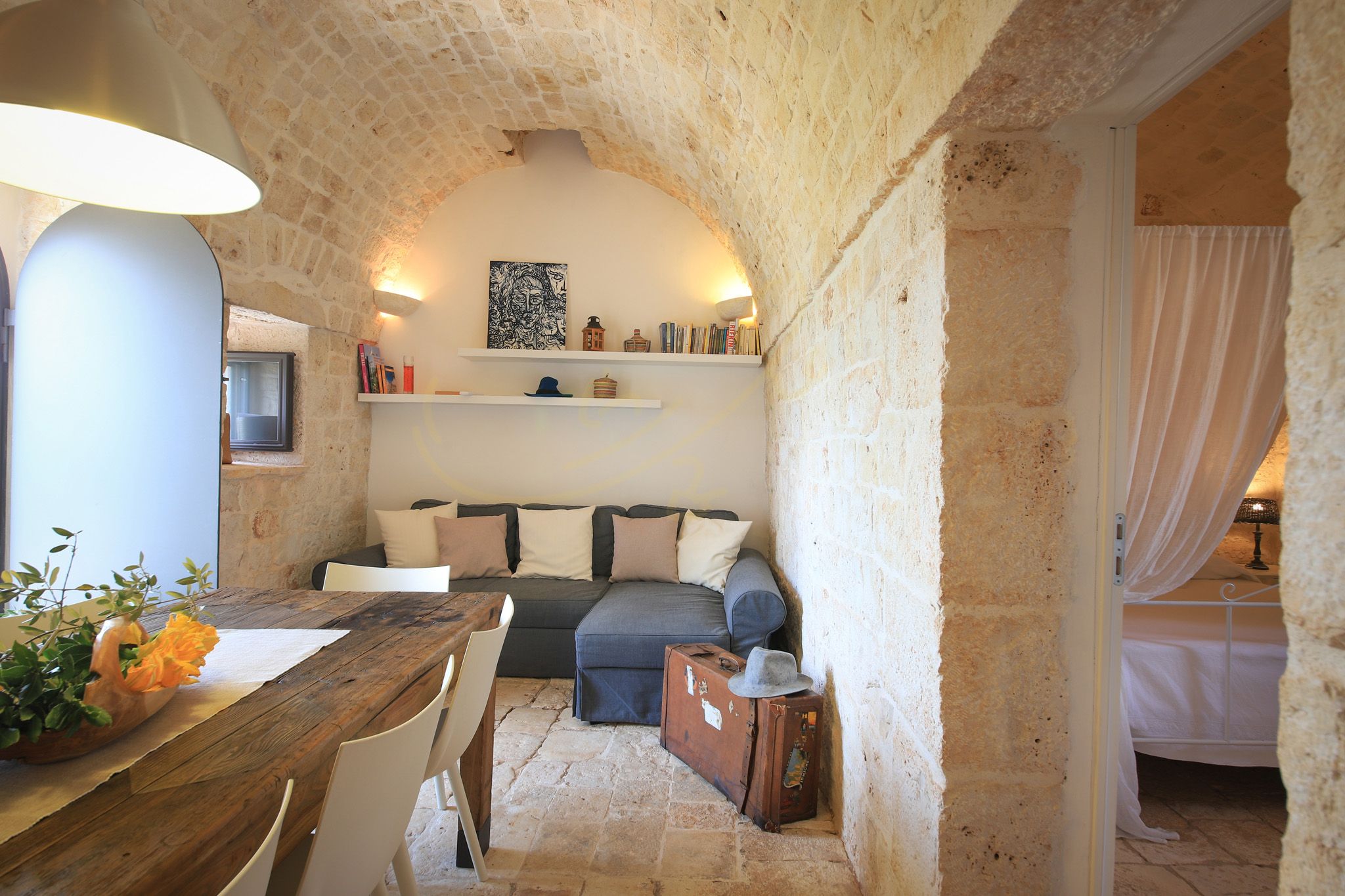 Une pièce chaleureuse avec un mur en pierre, une table en bois, un canapé et un lit à baldaquin.