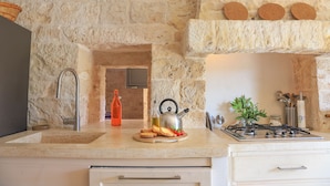 A kitchen with a stone wall, a sink, a stove, and a countertop with a cutting board, a kettle, and a bottle. - TD Casale Terranova Stone Farmhouse with Pool (Monopoli)