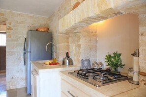 A kitchen with a stone wall, a stainless steel refrigerator, a gas stove, and a sink. - TD Casale Terranova Stone Farmhouse with Pool (Monopoli)