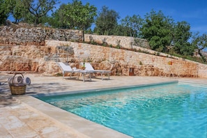 Uma piscina com espreguiçadeiras e um muro de pedra.