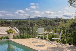 A poolside area with a table and chairs, surrounded by a fence, overlooking a landscape with trees and hills. - TD Casale Terranova Stone Farmhouse with Pool (Monopoli)
