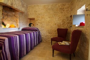A room with stone walls, a bed with striped bedding, a red chair, and a small shelf with a red hat. - TD Casale Terranova Stone Farmhouse with Pool (Monopoli)