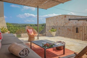 A balcony with a wicker chair, a table with fruits and a towel, and a view of a stone building and greenery. - TD Casale Terranova Stone Farmhouse with Pool (Monopoli)