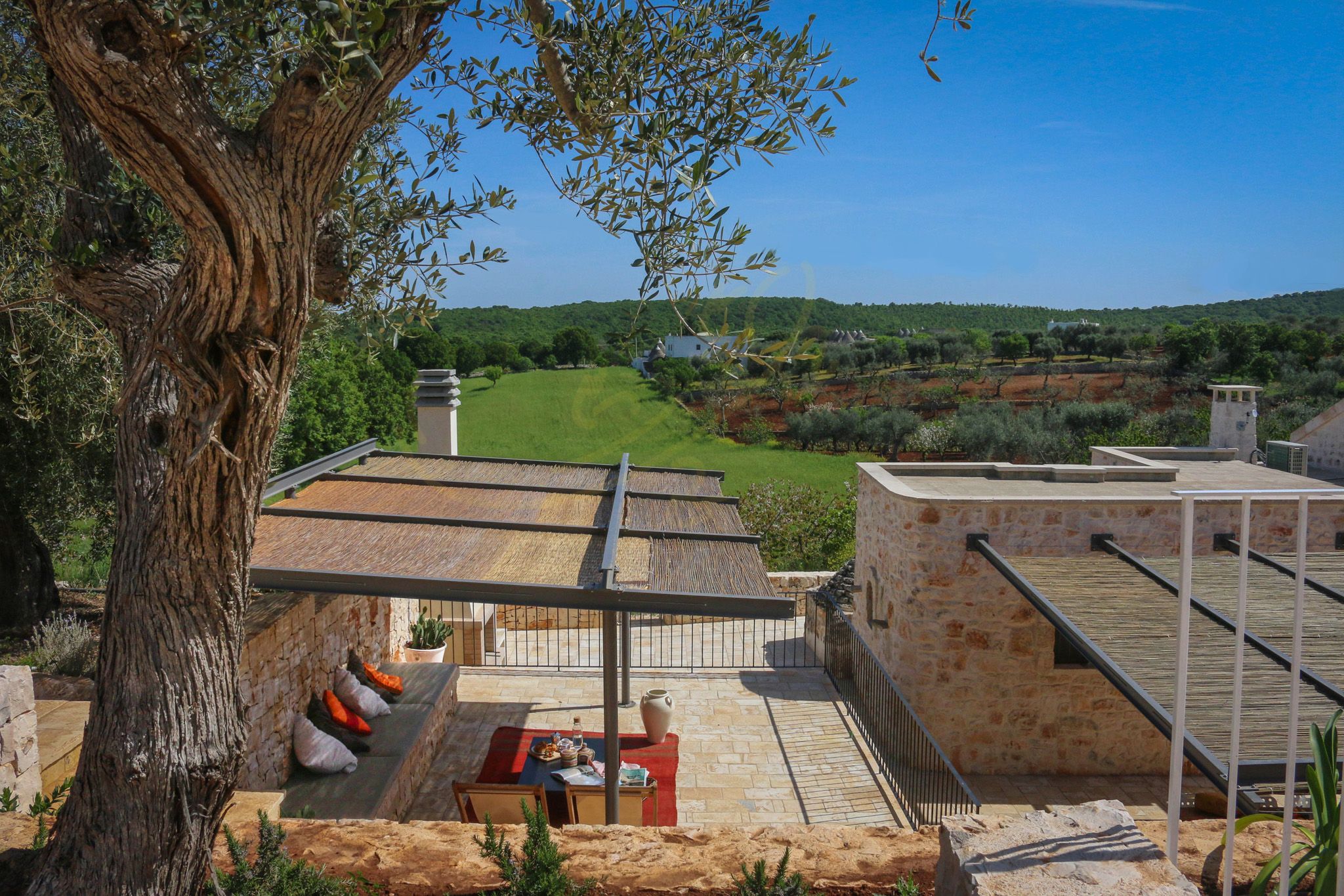 A terrace with a table and chairs, overlooking a green landscape and a clear sky.