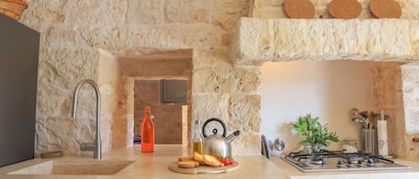 A kitchen with a stone wall, a sink, a gas stove, and a countertop with food items.