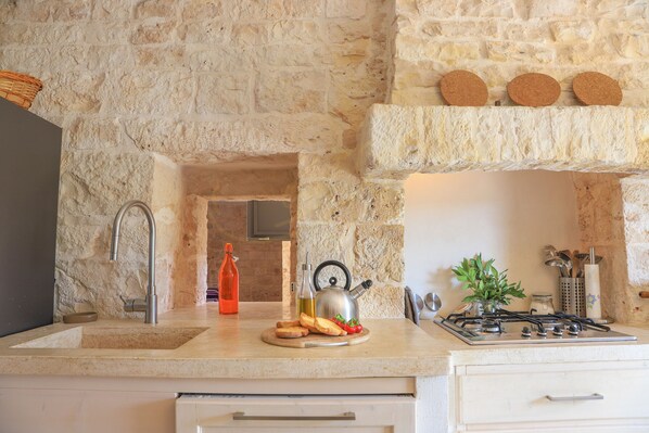 Una cocina con pared de piedra, un fregadero, una estufa a gas y una encimera con alimentos.