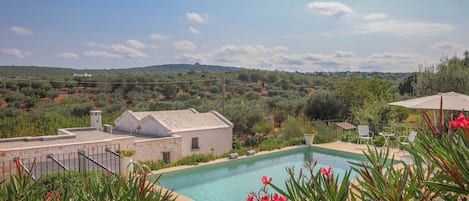 Piscina com vista para uma paisagem montanhosa, cercada por vegetação e um edifício branco.