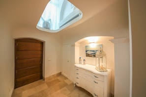 A hallway with a wooden door, a white dresser with drawers, a painting, and a skylight.