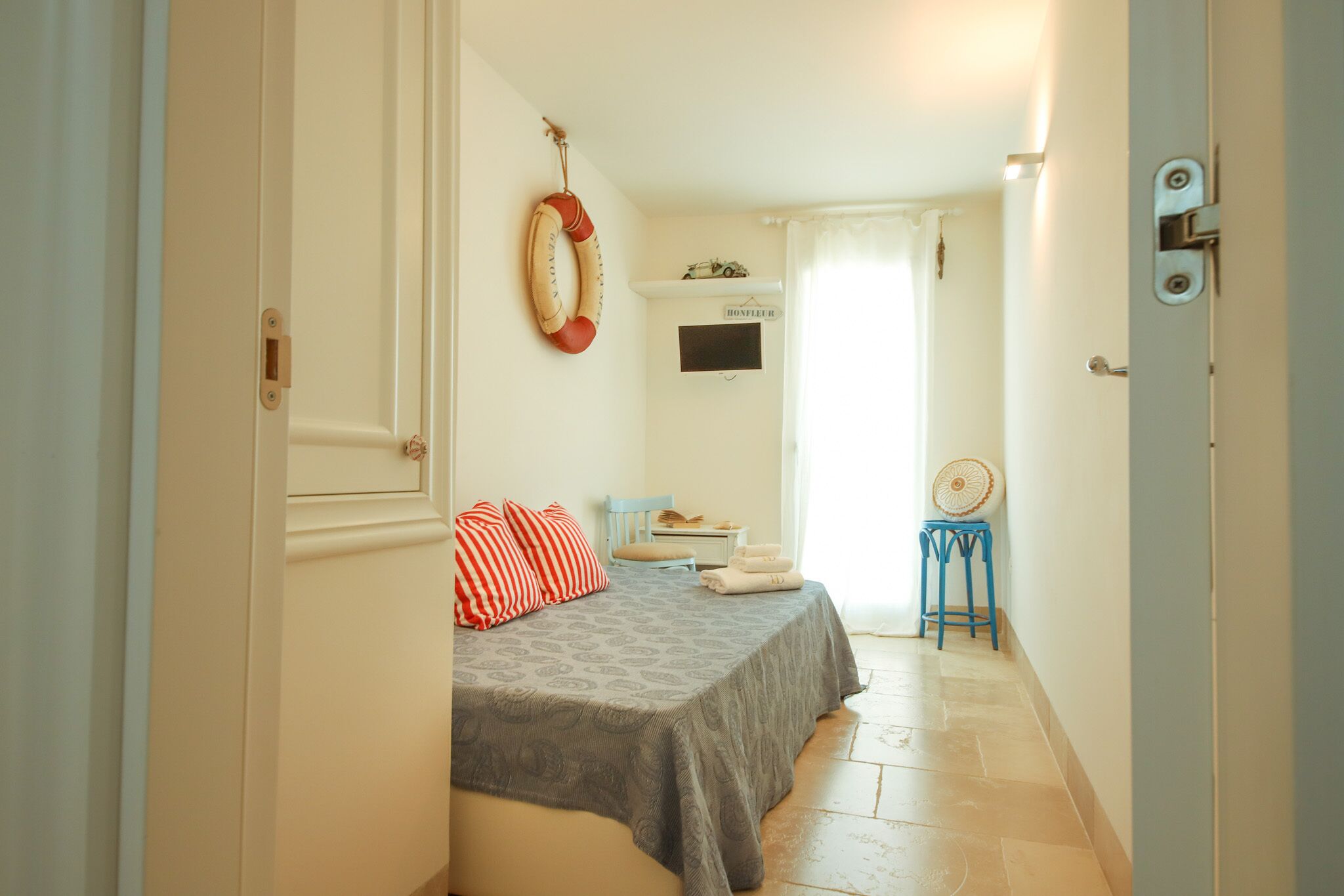 A bedroom with a bed, a chair, a small table, and a wall-mounted TV.