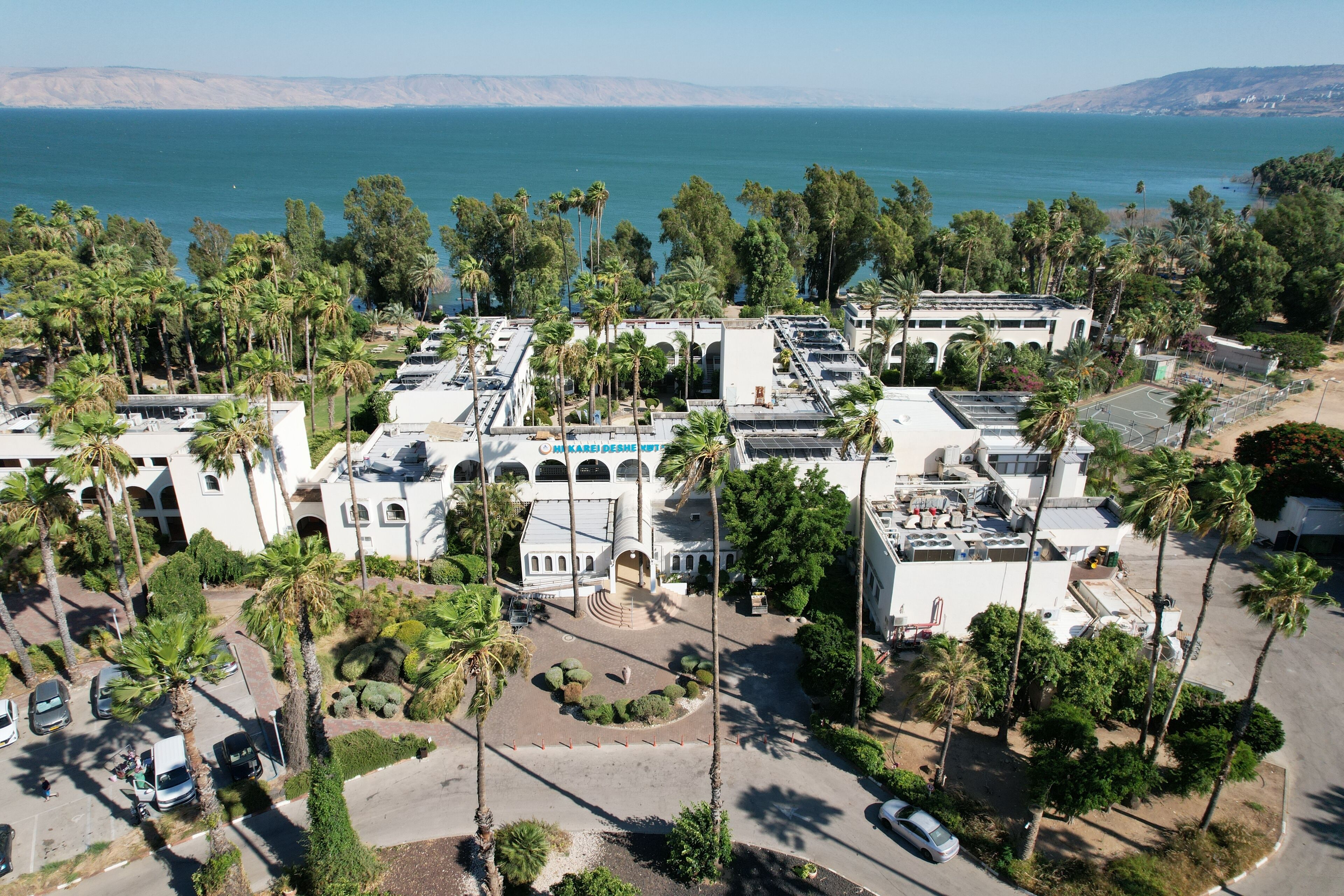 An aerial view of a resort with a pool, palm trees, and a view of the ocean.