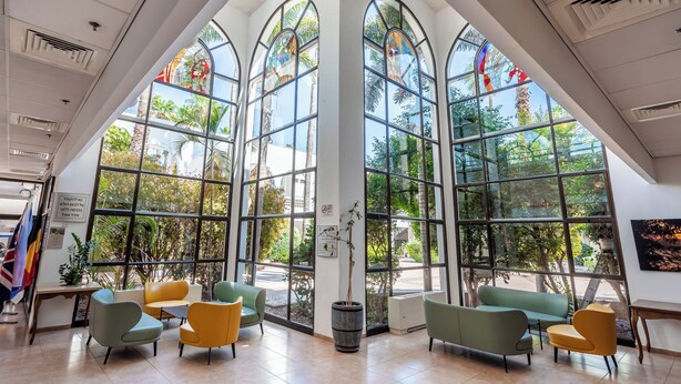 A spacious interior with large arched windows, multiple seating areas, and a potted plant. - HI Karei Deshe Hostel (Emek HaYarden)