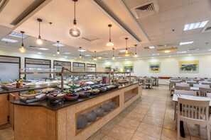 A buffet area with multiple food stations, a counter with various dishes, and a seating area with tables and chairs. - HI Karei Deshe Hostel (Emek HaYarden)