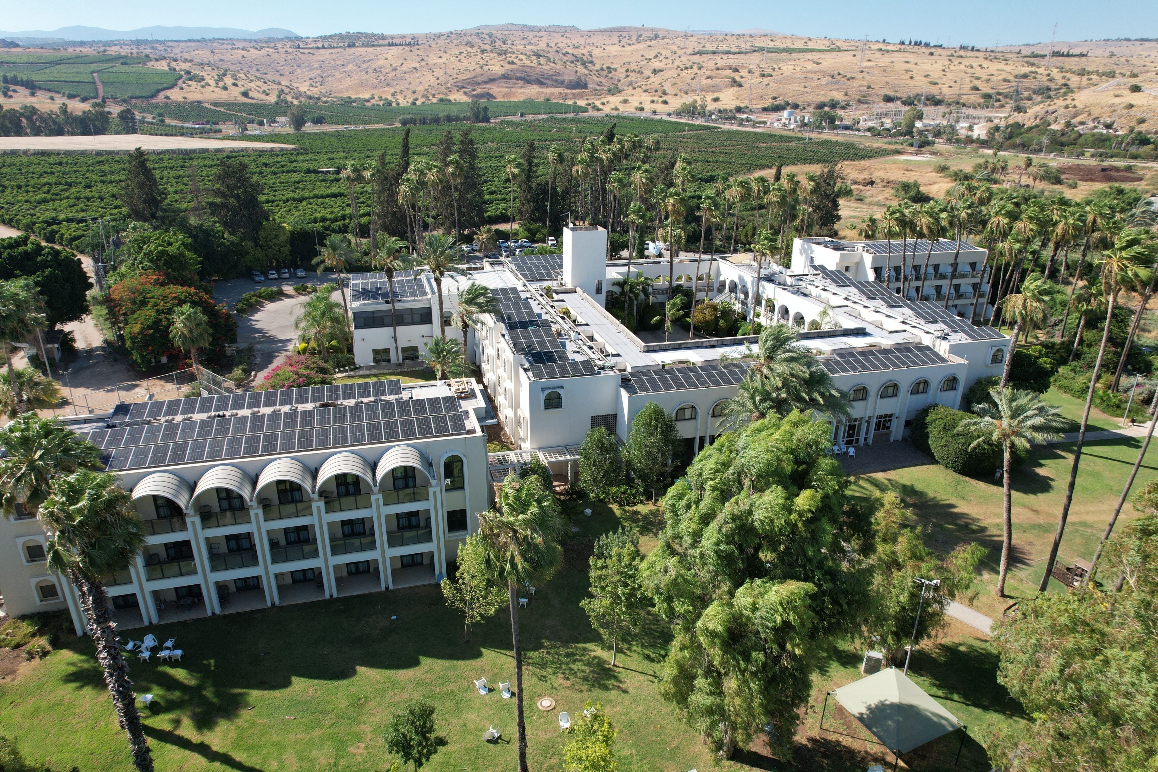 A hotel with multiple buildings, solar panels, and a surrounding landscape with greenery and hills.