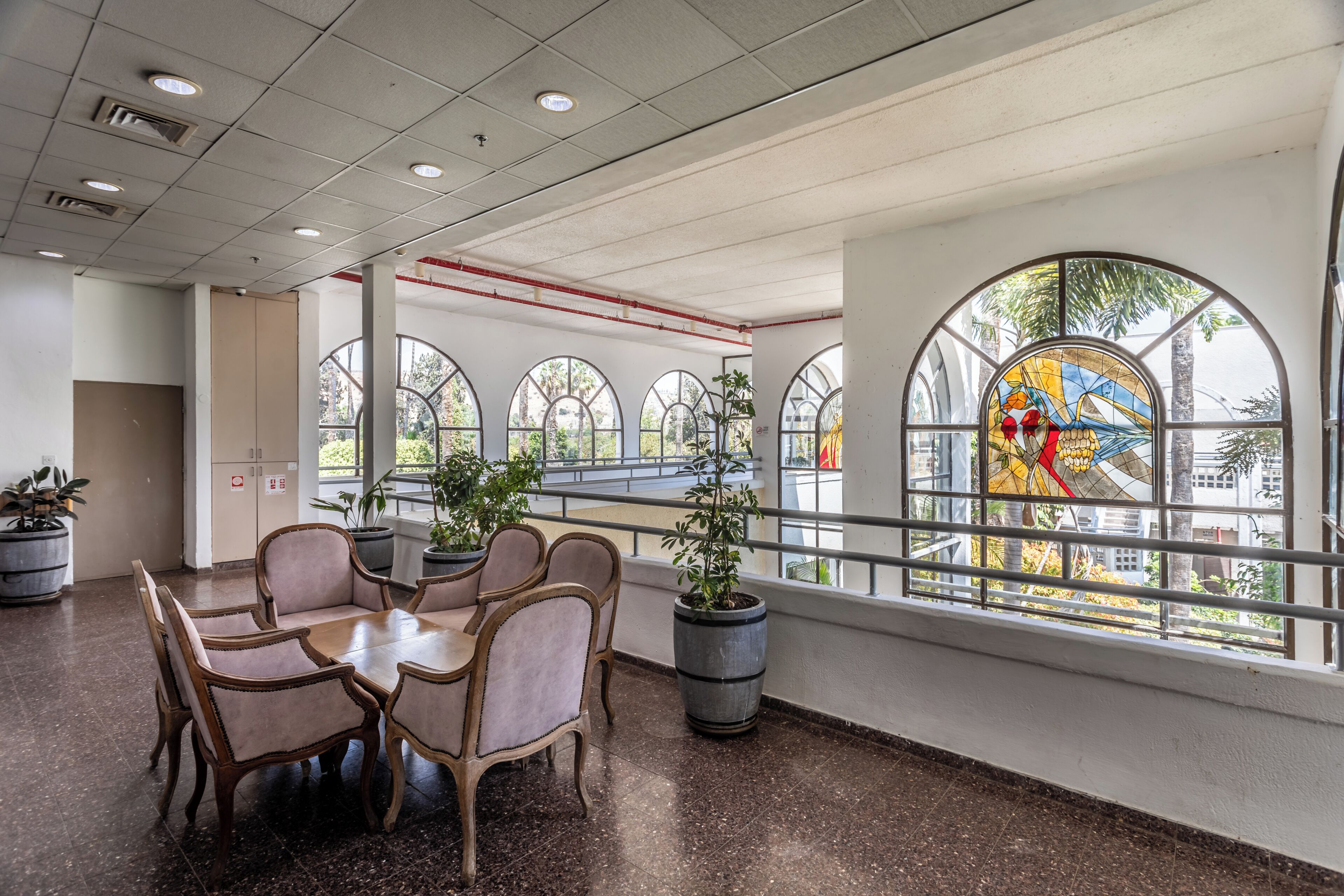 A dining area with a round table and chairs, potted plants, and large windows with arched designs.