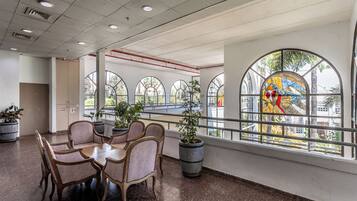 A dining area with a round table and chairs, potted plants, and large windows with arched designs.