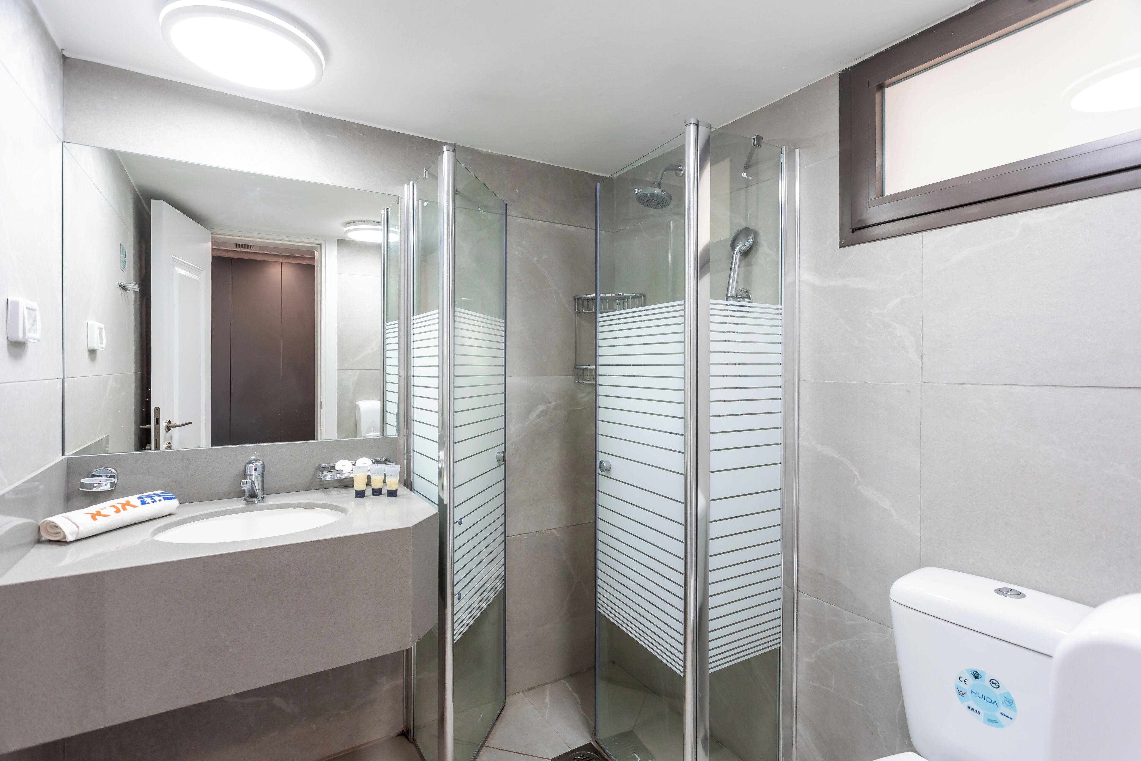 Une salle de bain moderne avec une douche à parois de verre, un lavabo avec un miroir et des toilettes ornées d’un autocollant bleu.