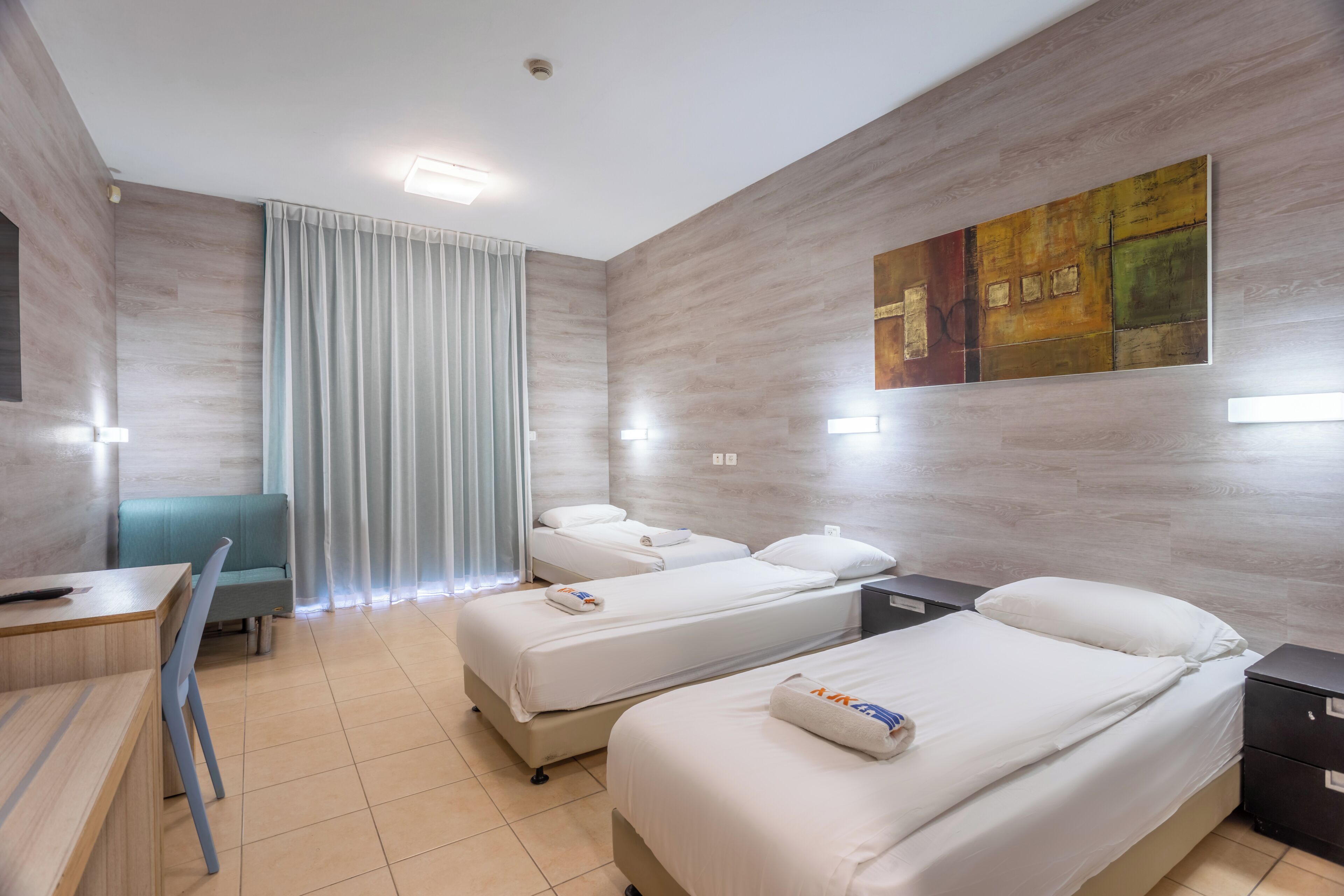 Habitación de hotel con dos camas, un escritorio, una silla y un cuadro grande en la pared.