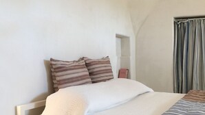 A neatly made bed with a white duvet and patterned pillows, a white lace bed skirt, and a striped blanket. - Dimora Casalino (Ostuni)