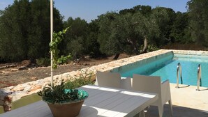 A poolside area with a table and chairs, a potted plant, and a pool. - Dimora Casalino (Ostuni)