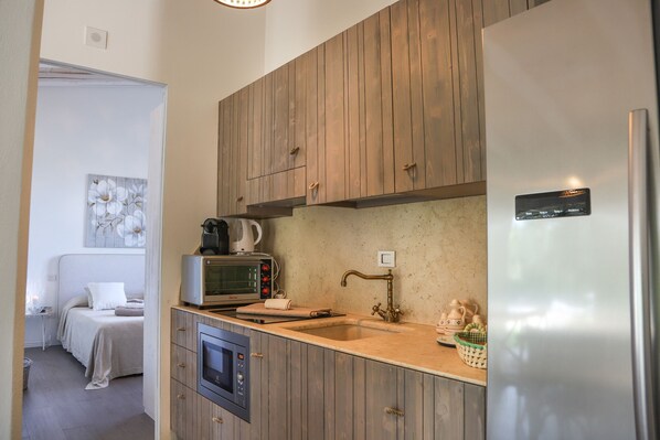 A compact kitchen with wooden cabinets, a built-in microwave, a stainless steel refrigerator, and a small sink. - TD Il Vecchio Fienile Outdoor Kitchen with Pool View (Polignano a Mare)