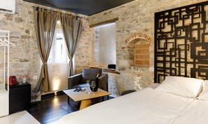 Une pièce avec un mur en pierre, un lit, une table avec des verres et une bouteille, et une chaise.