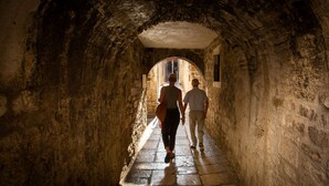 A narrow stone corridor with an arched ceiling, leading to a brighter area with a window. - Palace Luxury Room (Split)