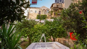 A courtyard with a water feature, greenery, and a building with stone walls in the background. - Palace Luxury Room (Split)