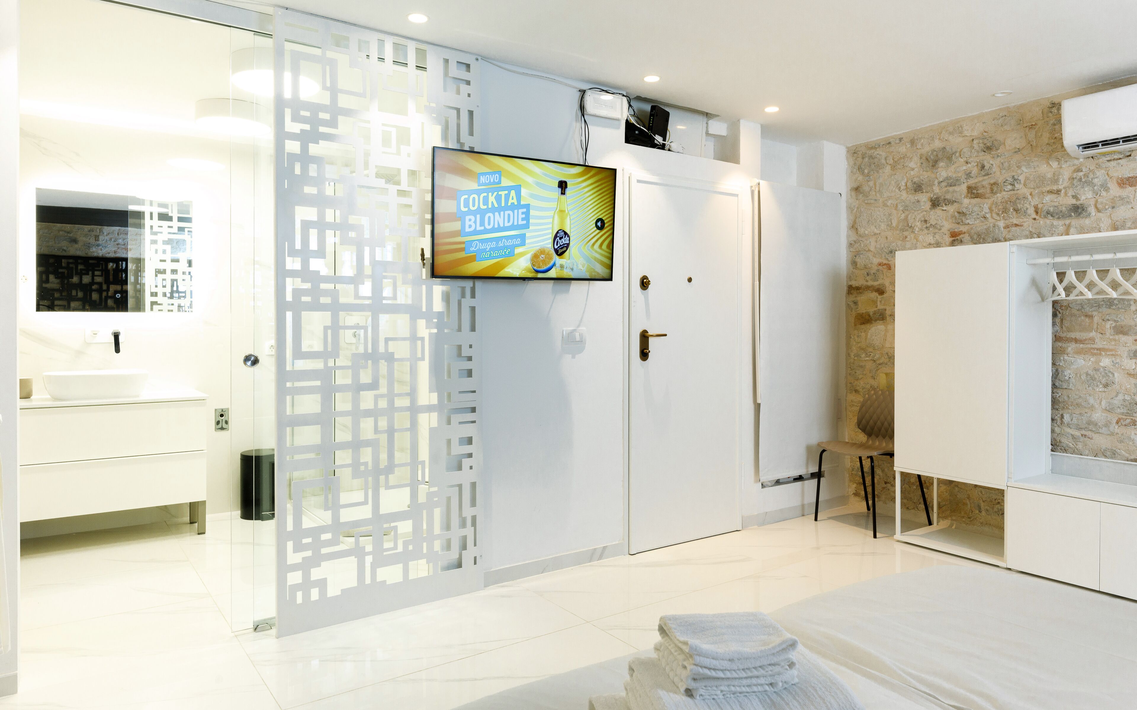 A modern bathroom with a large mirror, a sink, a toilet, and a shower area. There is a television mounted on the wall displaying an advertisement.