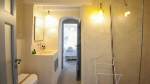 Une petite salle de bain comprenant des toilettes, un lavabo et un miroir. On peut voir un porte-serviettes et un espace douche.