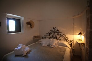 A bedroom with a bed, a window, a wall-mounted hat, and a bedside lamp. - Trulli della Contessa (Monopoli)