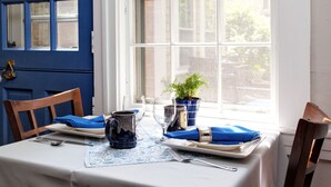 A dining table set with blue napkins, a pitcher, and a plate, with a window in the background.