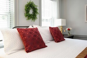 A neatly made bed with white and red patterned pillows, a bedside lamp, and a small vase with flowers. - Inn on Main (Yarmouth Port)