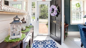 A foyer with a dark wooden door, a blue and white patterned rug, a white bench, and a mirror with ornate detailing.