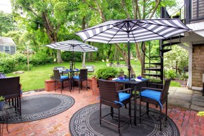 An outdoor patio with wicker furniture, striped umbrellas, and a brick floor. - Inn on Main (Yarmouth Port)