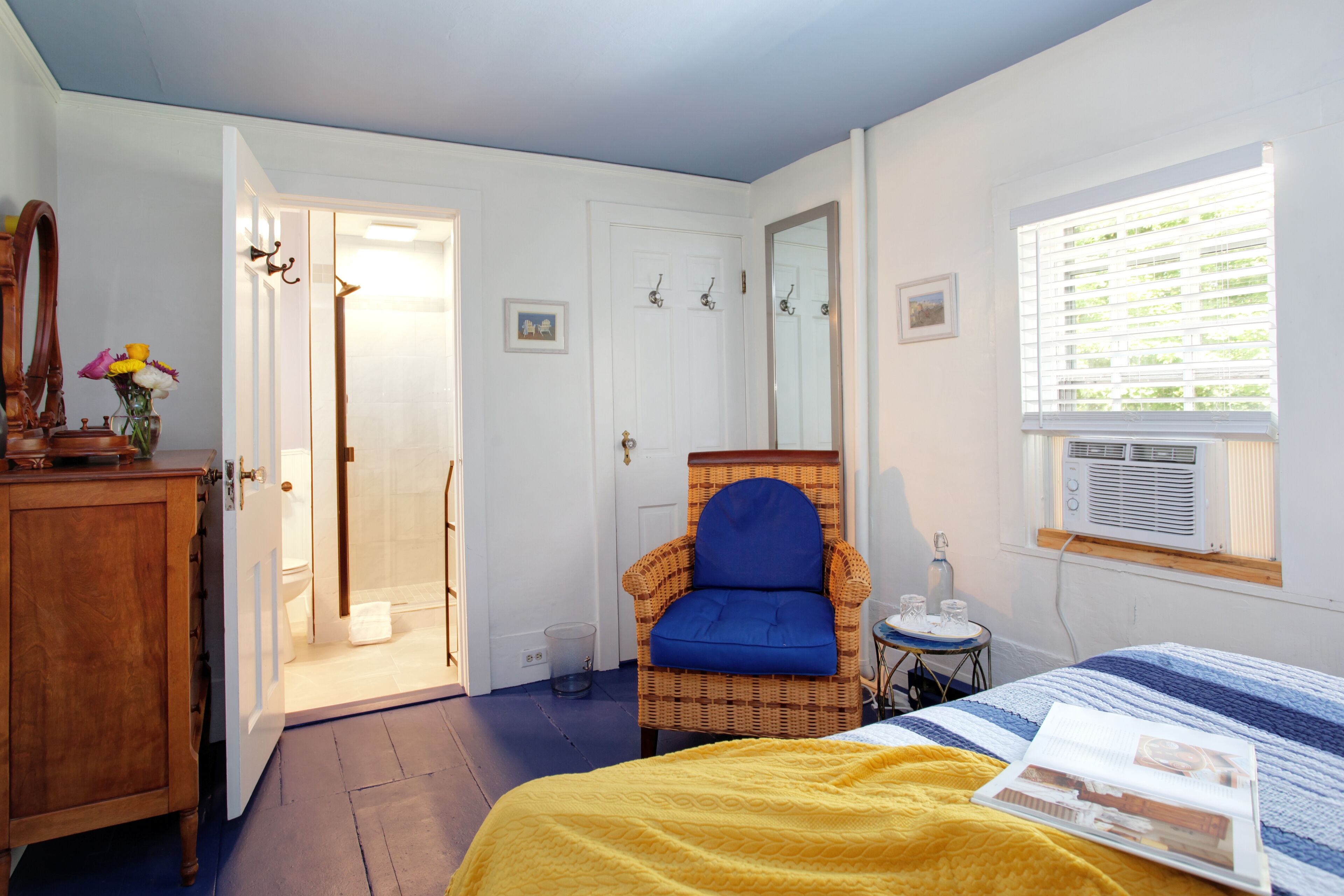 A bedroom with a bed, a chair, a dresser, a window with blinds, and a door leading to another room.
