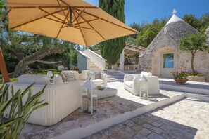 A stone building with a conical roof, a staircase leading to a door, and outdoor seating with cushions and a table. - TD Trulli di Bouganville w/ Large Amazing Pool (Monopoli)