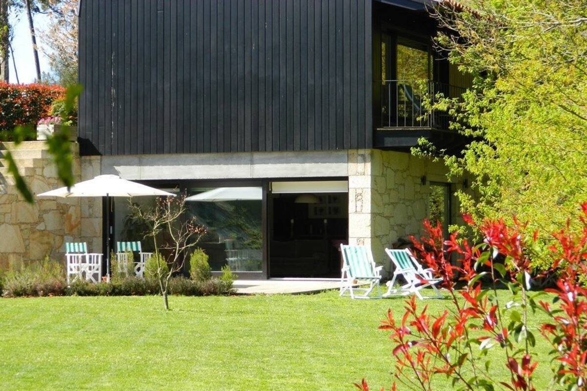 Una casa moderna con fachada de piedra, un balcón y un césped bien cuidado con mobiliario exterior.
