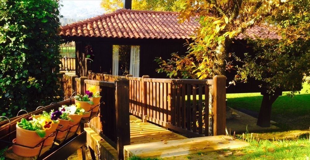 Un pont en bois menant à un bâtiment doté d’un toit en tuiles, entouré de verdure et de plantes en pot.