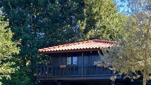 A wooden house with a red-tiled roof, a balcony, and a garden with various plants and flowers.
