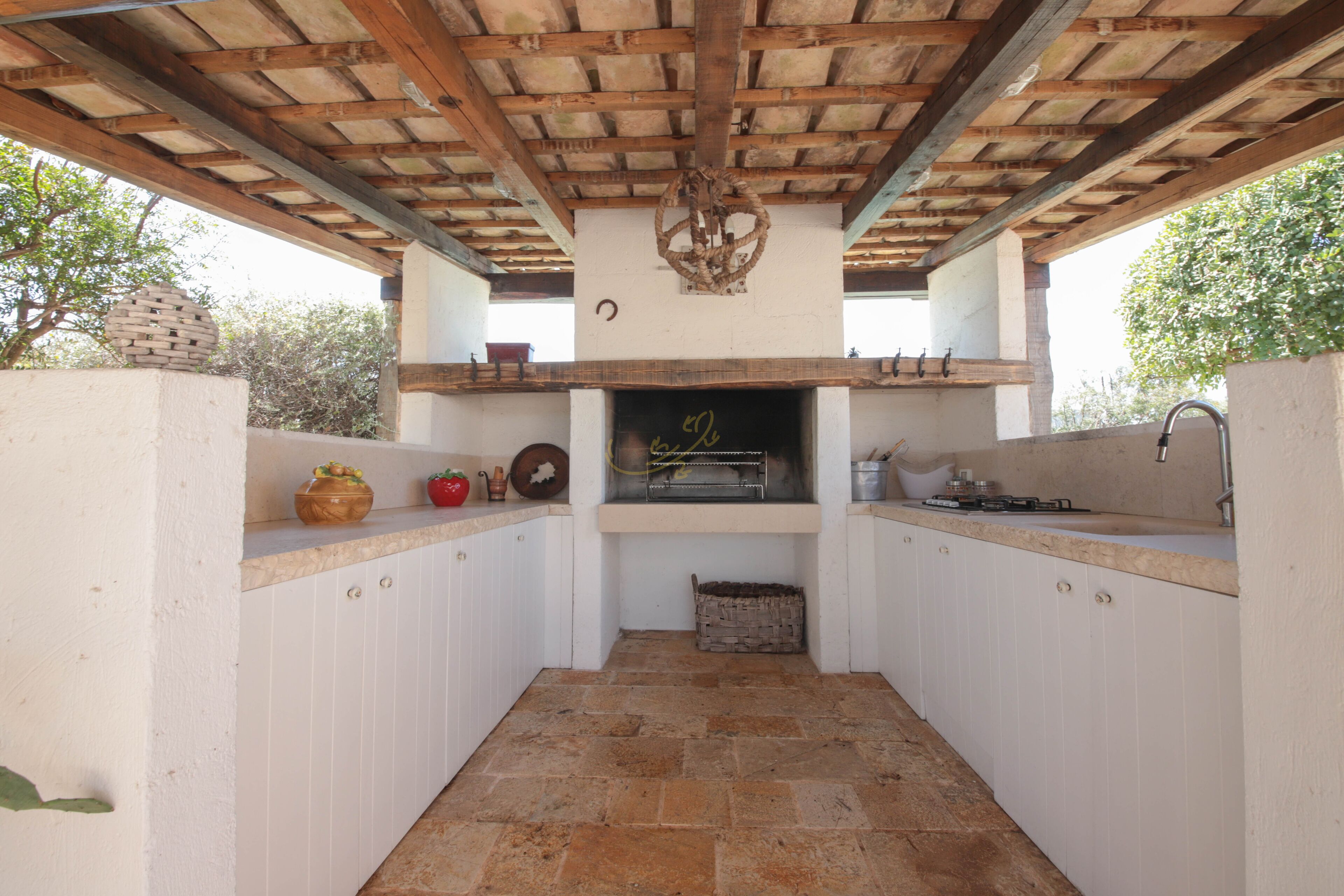 A compact kitchen with white cabinets, a stone-tiled floor, a built-in oven, and a hanging light fixture.