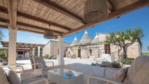 An outdoor seating area with wicker furniture and a glass table, overlooking a stone building with conical roofs. - TD Trulli di Montaltino with Stunning Huge Pool (Polignano a Mare)