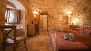 A stone-walled room with a bed, a wooden chair, a small table, and a radiator. - TD Trulli di Montaltino with Stunning Huge Pool (Polignano a Mare)