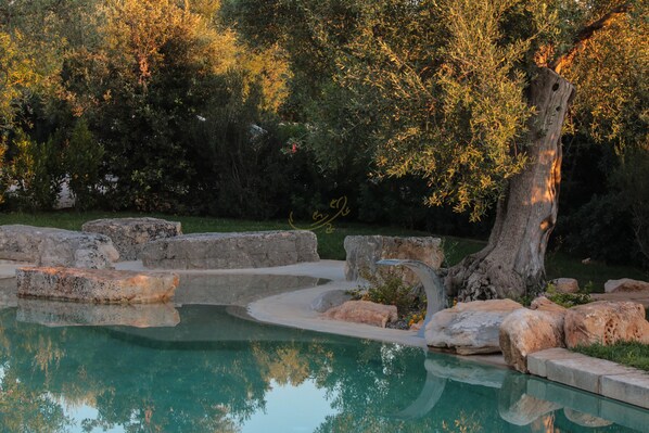 A swimming pool with a natural landscape, including rocks and trees. - TD Trulli di Montaltino with Stunning Huge Pool (Polignano a Mare)