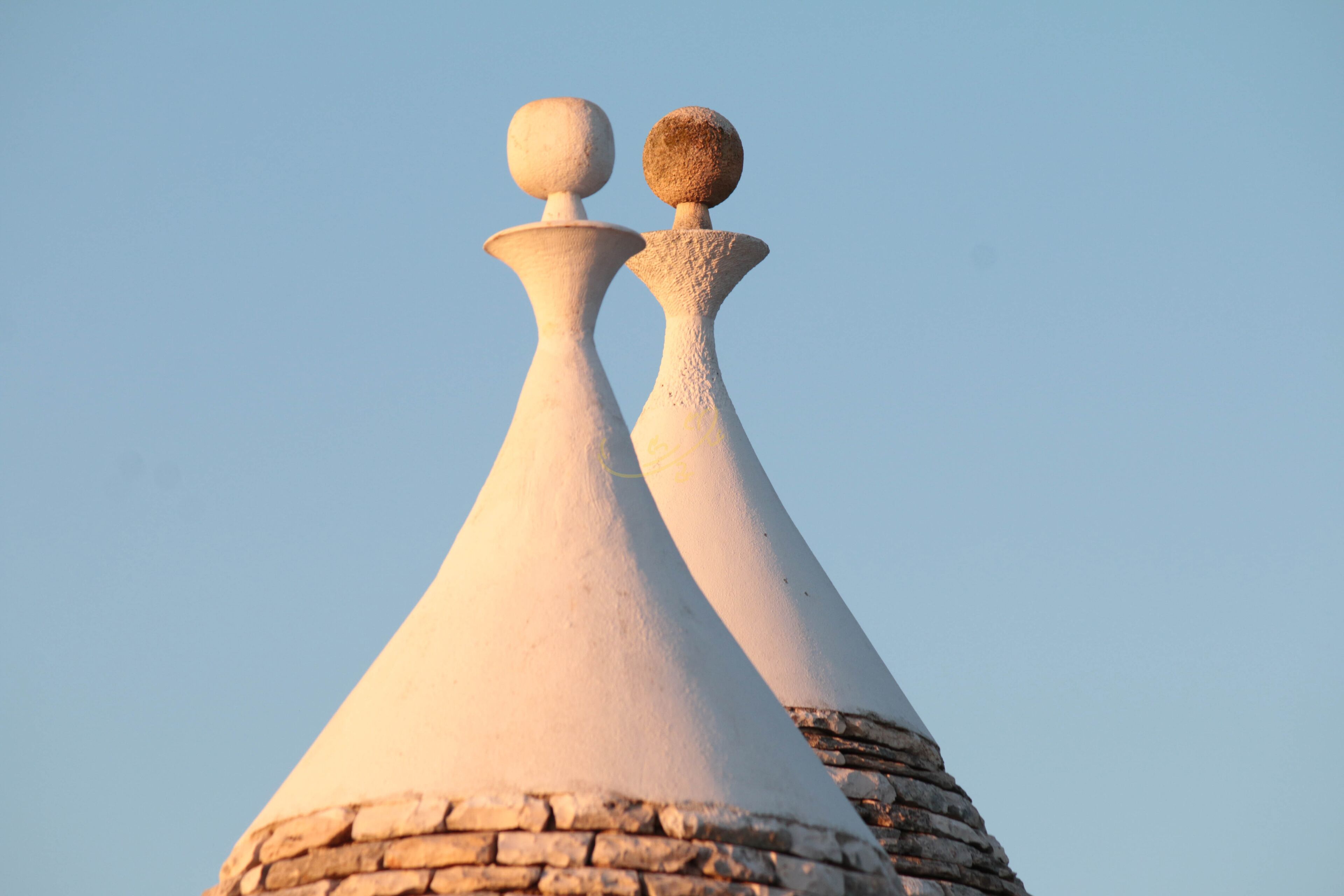 Two white conical structures with spherical tops against a clear sky.