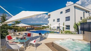 Un espace piscine extérieur moderne, doté de chaises longues, de parasols et d’un jacuzzi.