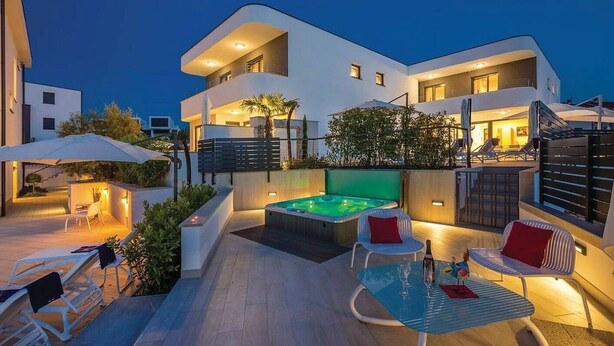 Un bâtiment moderne à deux étages doté d’un patio sur le toit, comprenant un jacuzzi, des sièges d’extérieur et un éclairage d’ambiance.